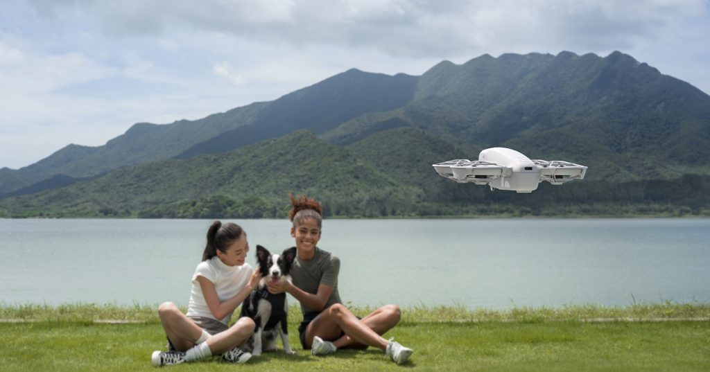 Zwei Frauen mit Hund lassen sich von DJI Neo Drohne am See filmen